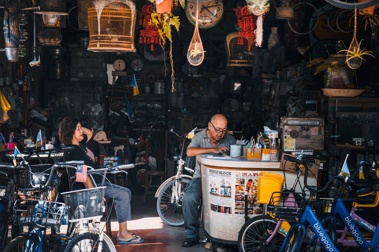 services-06 A bustling vintage bicycle shop with busy locals, set in an eclectic urban marketplace filled with old-world charm.